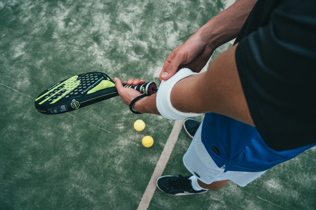 henkilö padel maila kädessä ja maassa kaksi tennispalloa